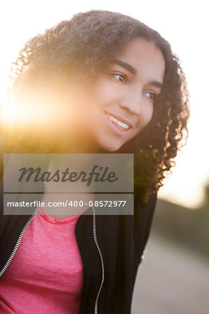 Outdoor sunset sunrise portrait with golden sunlight lens flare of beautiful happy mixed race African American girl teenager female young woman smiling with perfect teeth