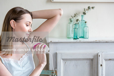 Woman using electric shaver to shave armpit