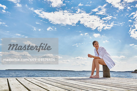 Young woman sitting on post on wooden pier, looking away