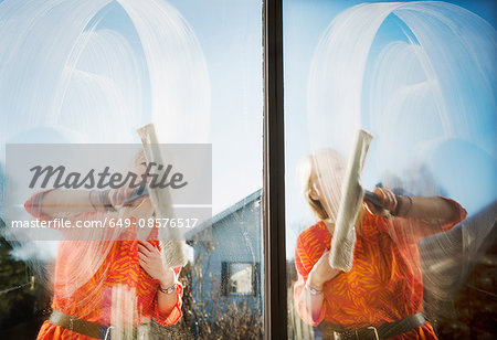 Composite of woman outdoors cleaning windows with squeegee