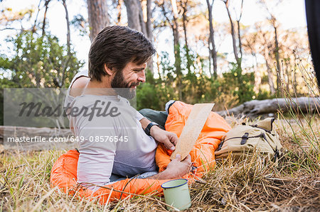 Man in sleeping bag reading map in forest, Deer Park, Cape Town, South Africa