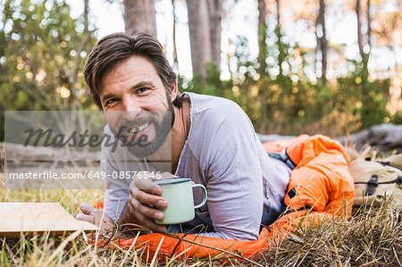 Portrait of man in sleeping bag with coffee in forest, Deer Park, Cape Town, South Africa