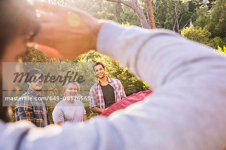 Over shoulder view of four men putting up tent in forest, Deer Park, Cape Town, South Africa