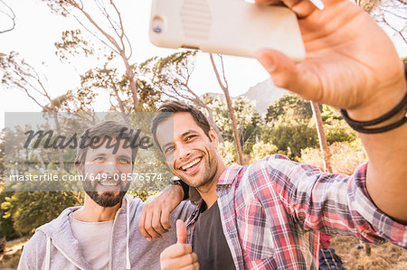 Two men taking smartphone selfie whilst camping in forest, Deer Park, Cape Town, South Africa