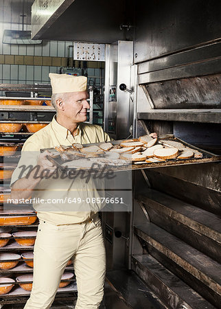 Happy baker placing tray of sliced bread into oven