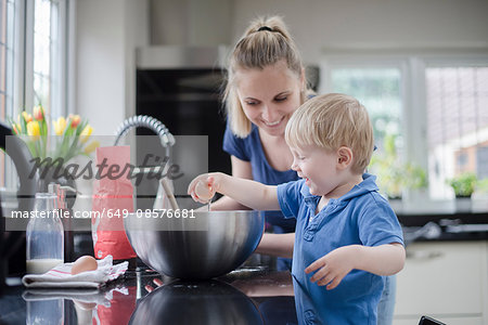 Mother helping son bake cake, son cracking egg