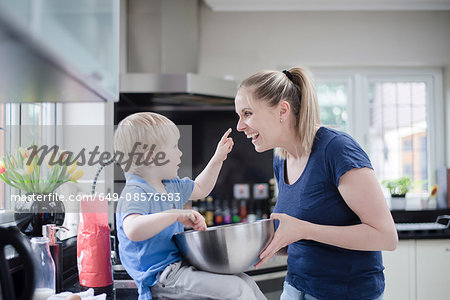 Mother and son fooling around whilst baking, son putting mixture on mother's nose