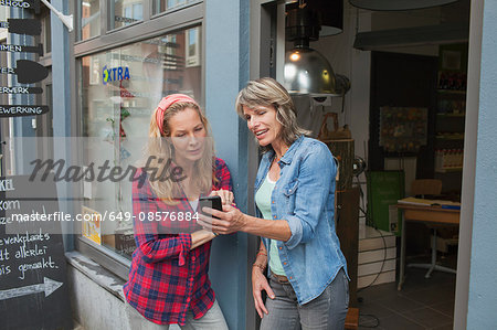 Women standing in shop doorway looking at smartphone