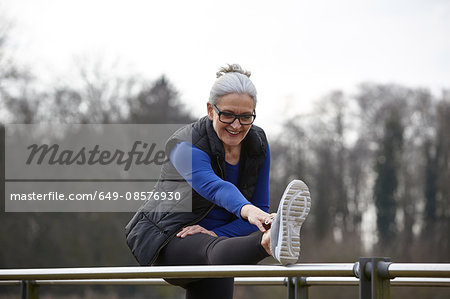Woman with leg raised on railing bending forward stretching