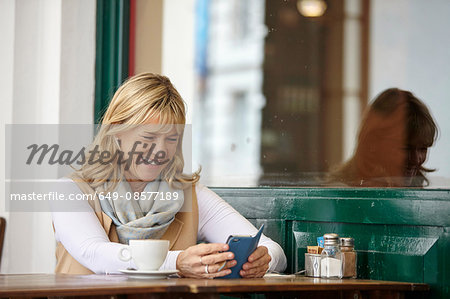 Mature woman reading smartphone text at sidewalk cafe table