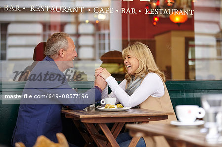 Mature dating couple holding hands at sidewalk cafe table