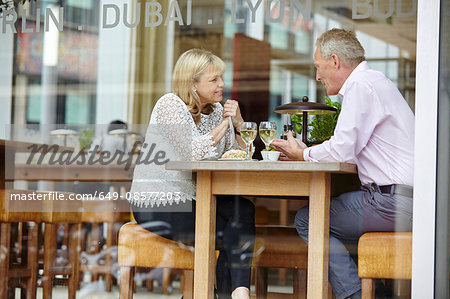 Window view of mature dating couple chatting at restaurant table