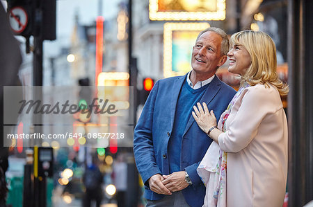 Mature dating couple looking up from city street at dusk, London, UK