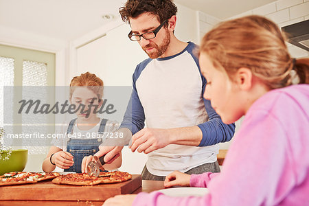 Mid adult man slicing pizza for daughters at kitchen bench