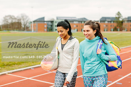 Two young women walking on running track, carrying sports bags
