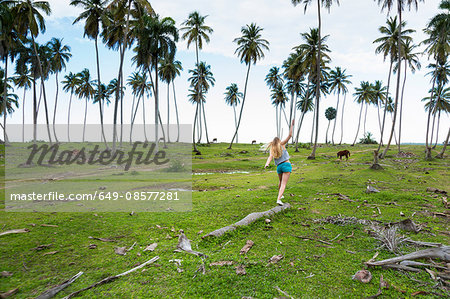 Young woman balancing on fallen tree trunk amongst palms, Dominican Republic, The Caribbean