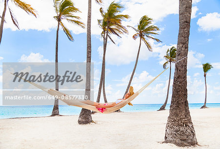 Young woman reclining in palm tree hammock at beach, Dominican Republic, The Caribbean