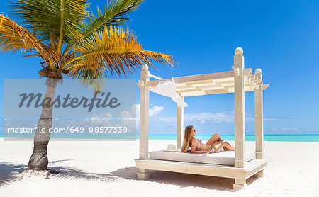 Young woman wearing bikini sunbathing on beach daybed, Dominican Republic, The Caribbean