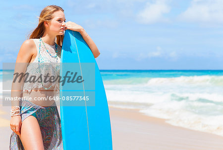 Young woman leaning against surfboard on beach, Dominican Republic, The Caribbean