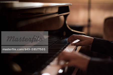 Hands of young man playing piano keys in bar at night