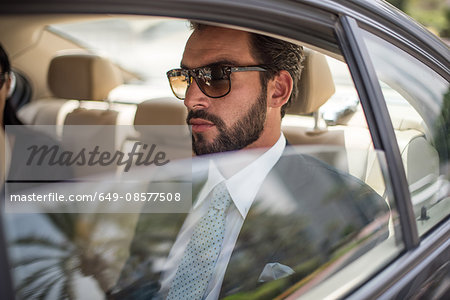 Young businessman wearing sunglasses in car backseat, Dubai, United Arab Emirates