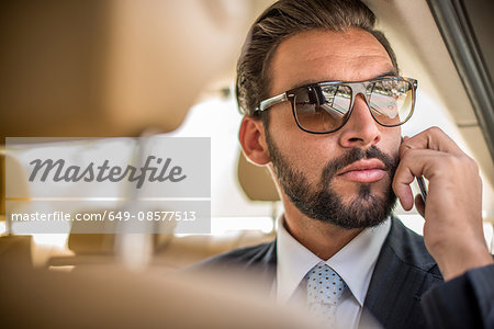 Young businessman wearing sunglasses talking on smartphone in car backseat, Dubai, United Arab Emirates Young businessman wearing sunglasses talking on smartphone in car backseat, Dubai, United Arab Emirates