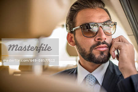 Young businessman wearing sunglasses talking on smartphone in car  backseat, Dubai, United Arab Emirates