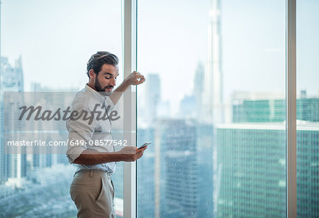 Businessman reading smartphone text at window with view of Burj Khalifa, Dubai, United Arab Emirates