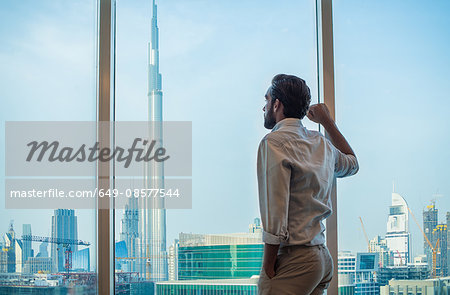 Businessman gazing through window with view of Burj Khalifa, Dubai, United Arab Emirates