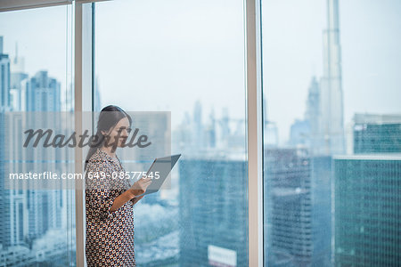 Businesswoman using digital tablet at window, Dubai, United Arab Emirates