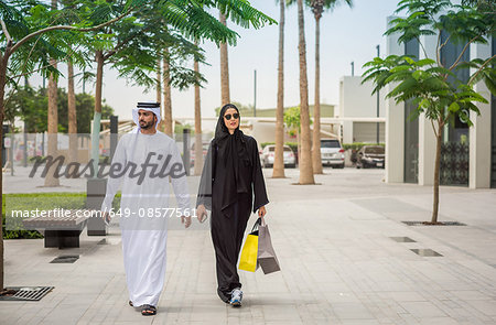 Middle eastern shopping couple  wearing traditional clothing walking along street, Dubai, United Arab Emirates