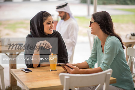Young middle eastern woman wearing traditional clothing talking with female friend at cafe, Dubai, United Arab Emirates