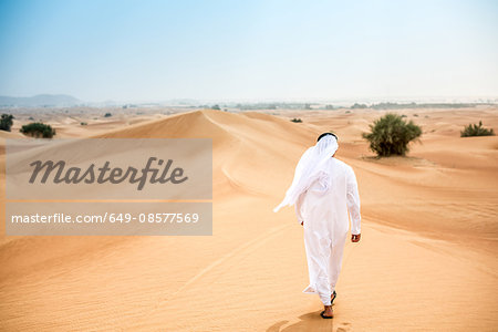 Rear view of middle eastern man wearing traditional clothes walking in desert, Dubai, United Arab Emirates