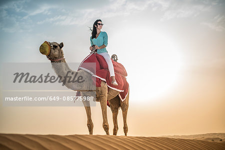Female tourist riding camel in desert, Dubai, United Arab Emirates