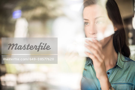 Woman drinking coffee at reflective cafe window, Dubai, United Arab Emirates