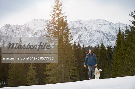Young man walking uphill with husky in snow covered landscape, Elmau, Bavaria, Germany