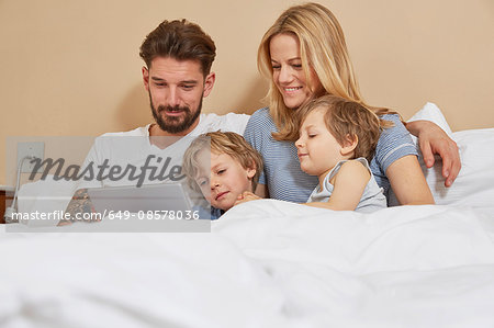 Mother and father in bed with sons looking at digital tablet Mother and father in bed with sons looking at digital tablet