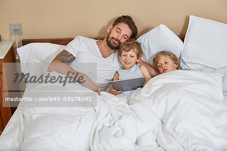 Father and sons in bed using digital tablet