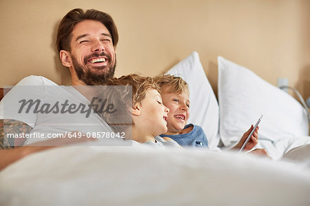 Father and sons in bed using digital tablet laughing