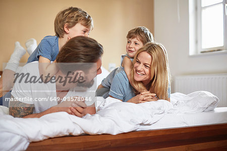 Boys on bed lying on top of parents face to face smiling
