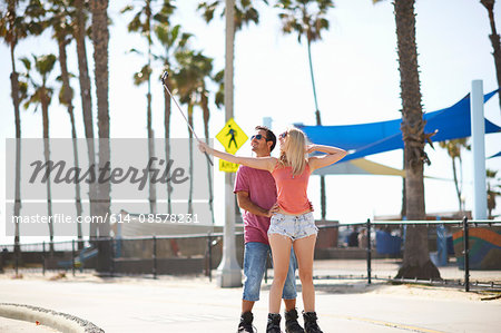 Couple rollerblading outdoors, taking self portrait, using selfie stick