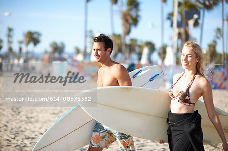 Surfing couple carrying surfboards on Venice Beach, California, USA