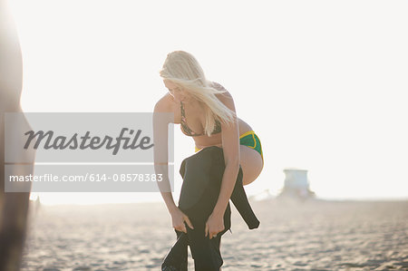 Young woman putting on wetsuit on Venice Beach, California, USA