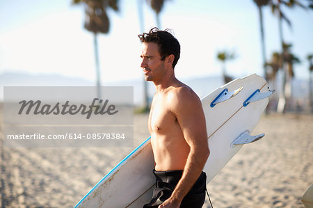 Male surfer carrying surfboard on Venice Beach, California, USA