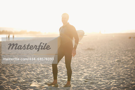 Male surfer carrying surfboard on sunlit Venice Beach, California, USA