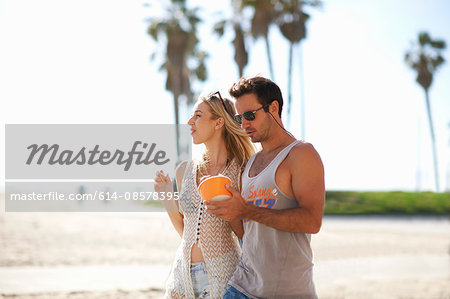 Couple strolling and sharing frozen yoghurt at Venice Beach, California, USA