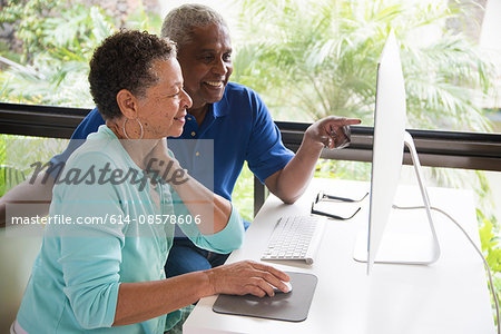 Senior couple sitting at table, using computer