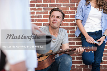 Pedestrian putting money in street musician's hat, mid section