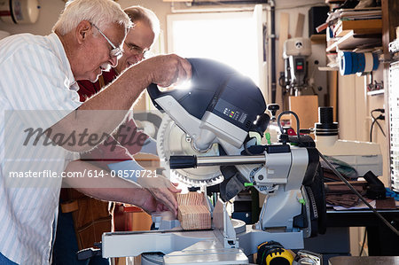 Senior men sawing on circular saw in carpentry workshop