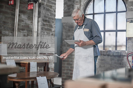 Senior craftsman preparing orders on digital tablet in antique restoration workshop